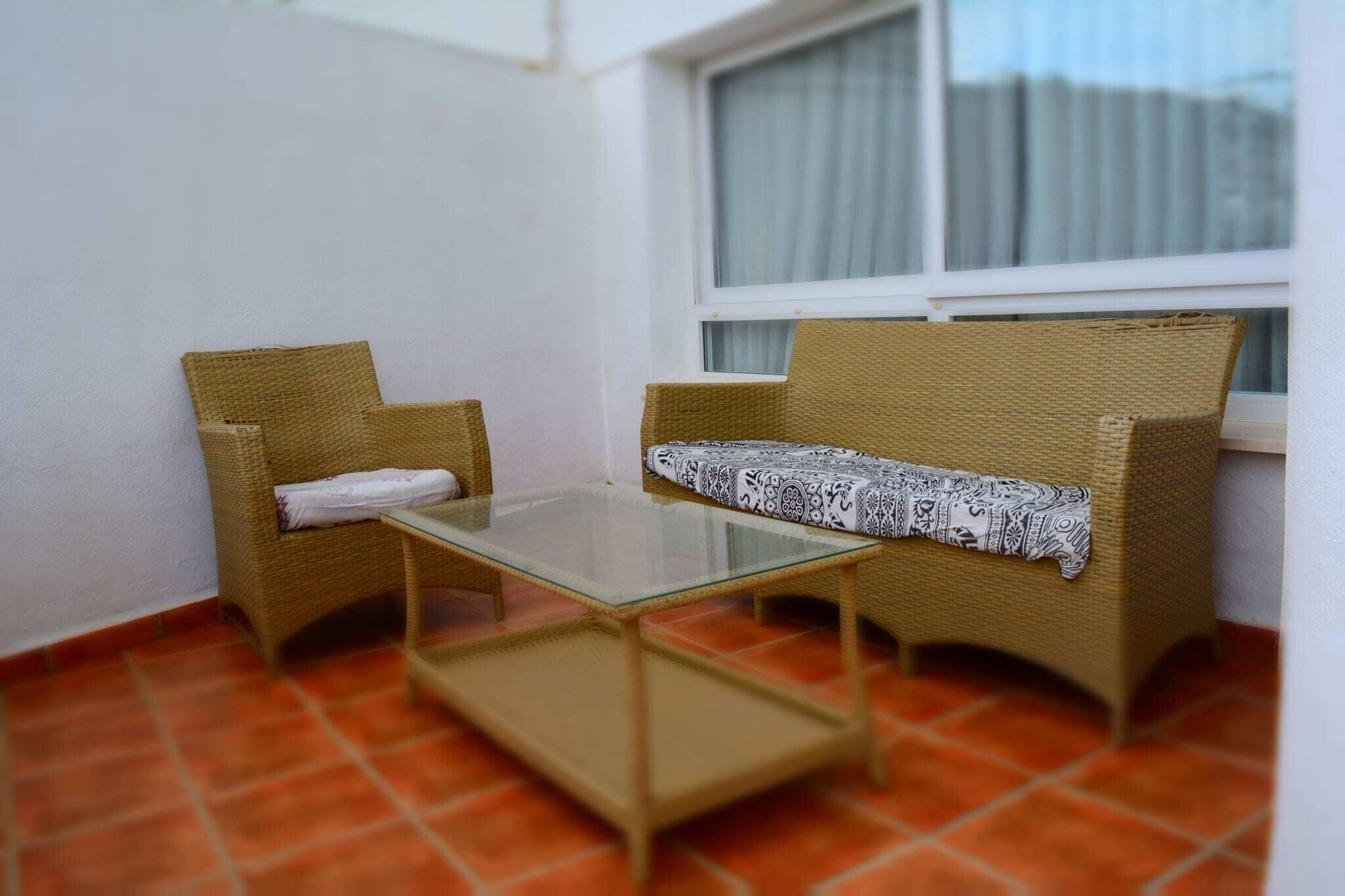 Un petit balcon agrémenté de meubles en osier, d’une table en verre et d’un coussin à motifs.