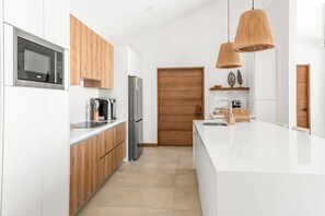 Eine moderne Küche mit weißen Schränken, einer Edelstahl-Mikrowelle, einer eingebauten Kaffeemaschine und einer Holztür.