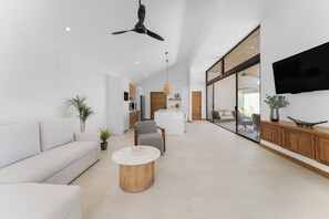 Ein modernes Wohnzimmer mit einer Couch, einem Couchtisch, einem Deckenventilator und einem an der Wand befestigten Fernseher.