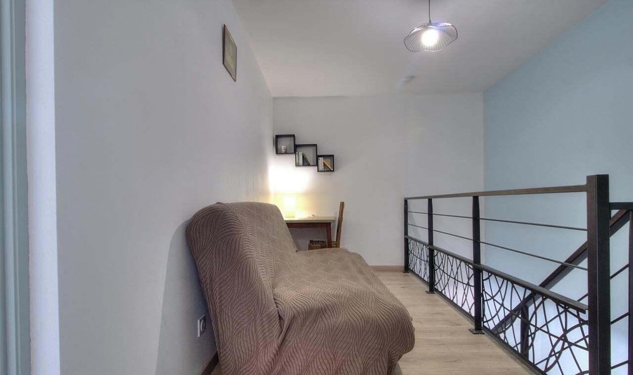 A staircase with a metal railing, a wall with framed pictures, and a bed with a blanket.