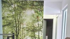 Quarto com uma cama grande, vista para uma floresta através de uma porta de vidro e escada que leva a um andar superior.