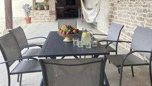 Pátio externo com mesa posta para refeições, ladeado por paredes de pedra e teto de madeira.