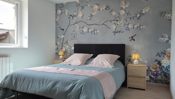 Quarto com cama, mesas de cabeceira, janela e um mural floral na parede.