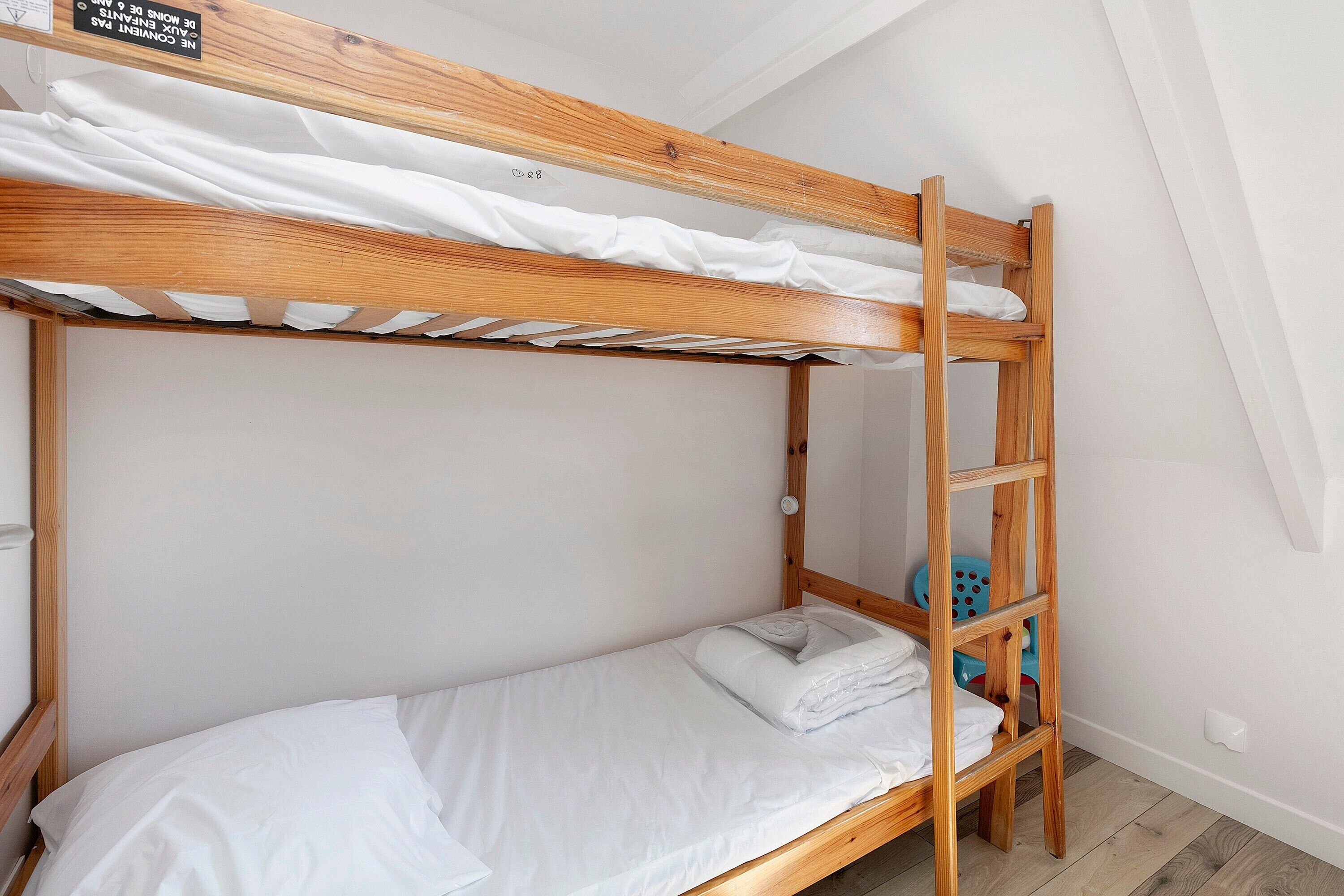 Ein Etagenbett mit Holzlade, weißer Bettwäsche und einem kleinen blauen Spielzeugstuhl.