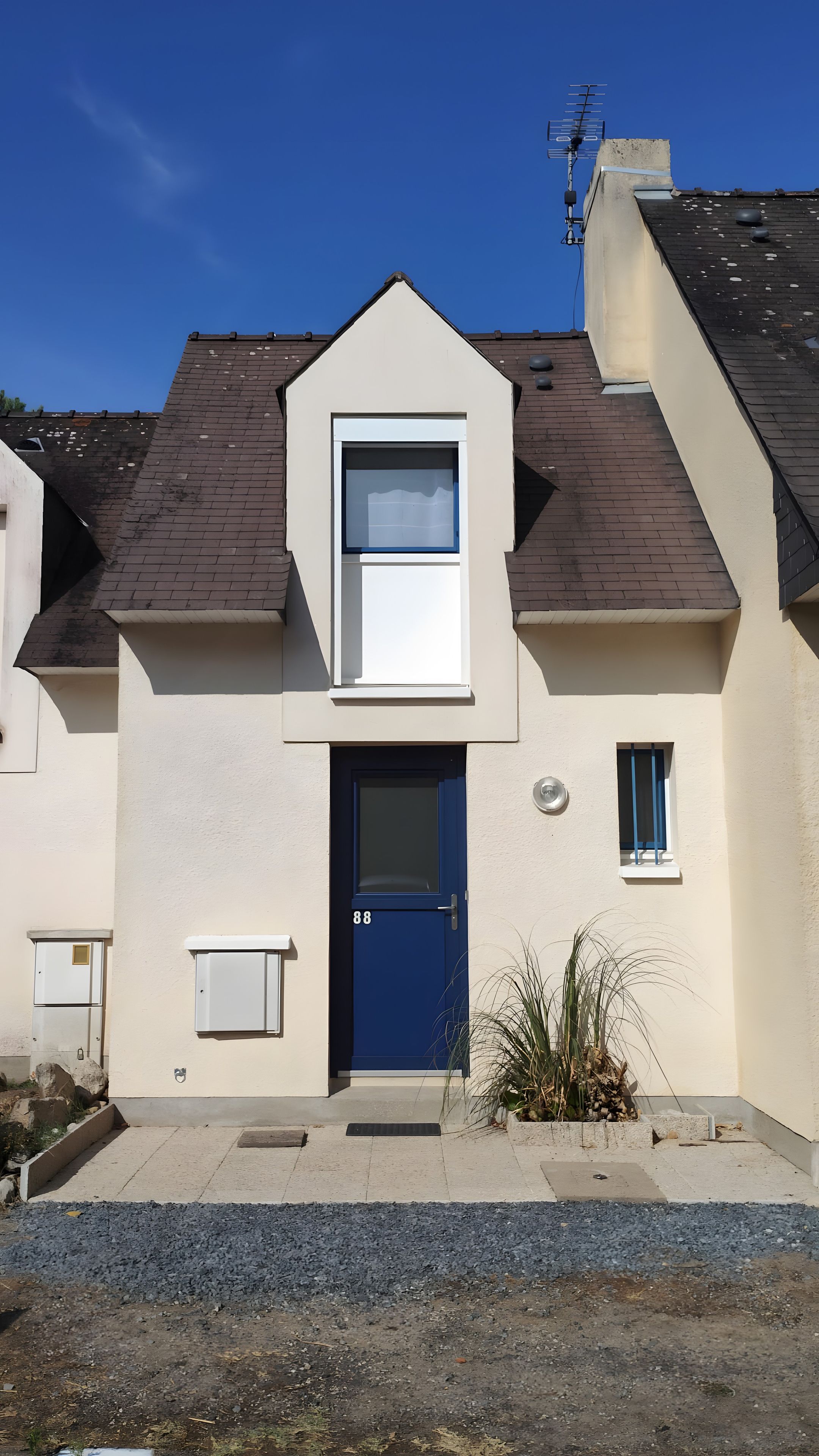 Une maison à deux étages avec une porte bleue, une petite fenêtre et une antenne parabolique sur le toit.