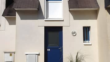 Une maison à deux étages avec une porte bleue, une petite fenêtre et une antenne parabolique sur le toit.