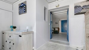 Une pièce avec un meuble blanc, une petite plante et une porte bleue qui donne sur une autre pièce.