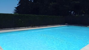 Une piscine rectangulaire à l’eau d’un bleu limpide, entourée d’une terrasse en béton et d’une haie basse.