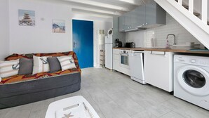 Une cuisine moderne avec des appareils électroménagers blancs, une porte bleue et un canapé gris agrémenté de coussins à motifs.