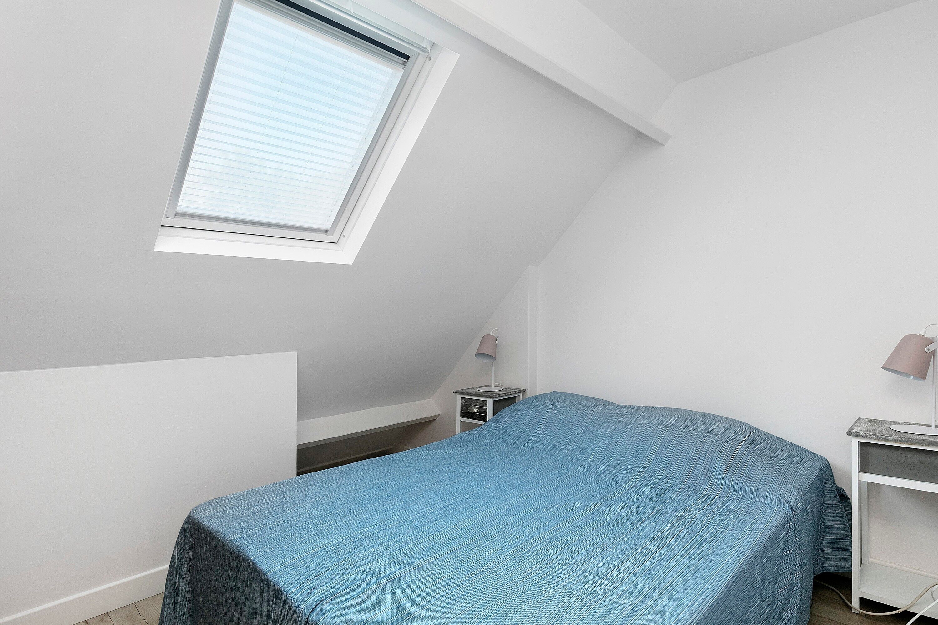 A small, simple room with a bed, a desk, a lamp, and a window.