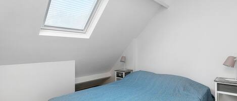 A small, simple room with a bed, a desk, a lamp, and a window.