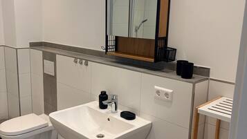 Un bagno moderno con un lavandino bianco, un water, uno specchio e uno scaffale con articoli da toilette.