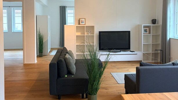 Ett modernt vardagsrum med en soffa, en tv och ett matbord i trä.
