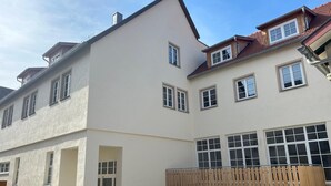 En byggnad med flera våningar, en slät fasad, stora fönster och ett trästaket framför.