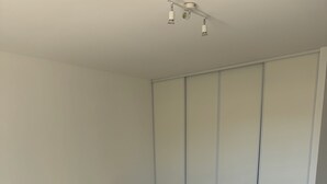 Un dormitorio con cama, piso de madera, paredes blancas y un armario.