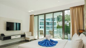 Camera d'albergo con un letto grande, una TV a schermo piatto, un'area salotto con poltrone e un balcone con vista sugli edifici.