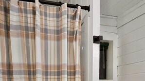A bathroom with a white toilet, a shower curtain with a plaid pattern, and a window with blinds. - Quiet Moose Cabin: 2-bedroom cabin, Mountain views, Hot tub for cozy getaway (Bailey)