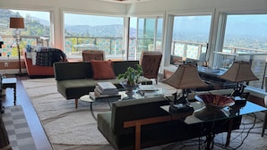 A spacious living room with a large window offering a city view, a sofa, a coffee table, and a lamp. - San Deigo Mountaintop Retreat -- SPECTACULAR! (La Mesa)