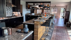 A modern kitchen with dark cabinetry, granite countertops, and a central island with bar stools. - San Deigo Mountaintop Retreat -- SPECTACULAR! (La Mesa)