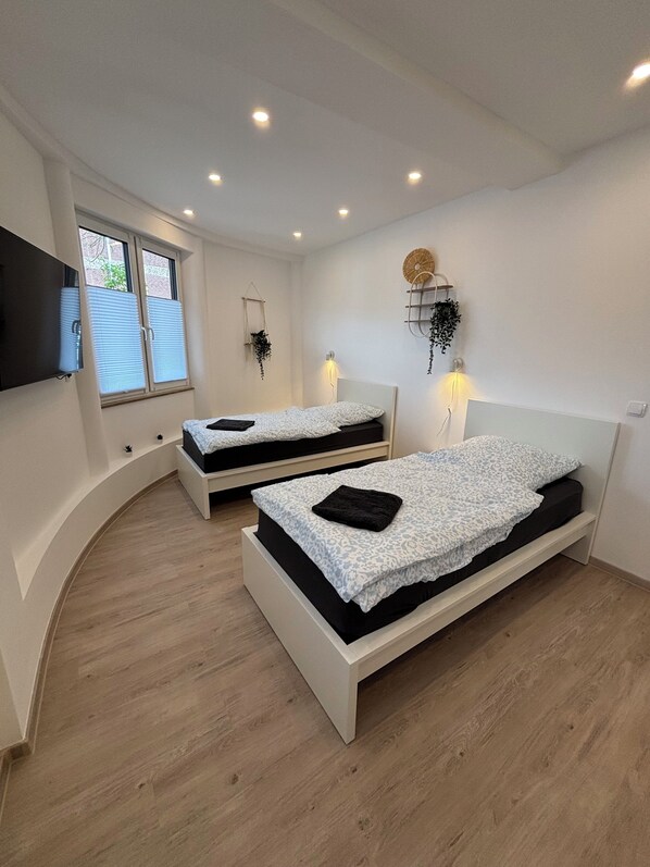 Ein modernes Schlafzimmer mit zwei Betten, einem Fernseher und einem Fenster mit Jalousien.