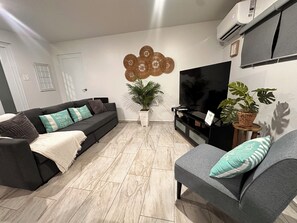 A living room with a sofa, a chair, a TV, a plant, and a wall-mounted air conditioner. - Escape to paradise with a private pool and home with a 3 min walk to the beach (Aguada)
