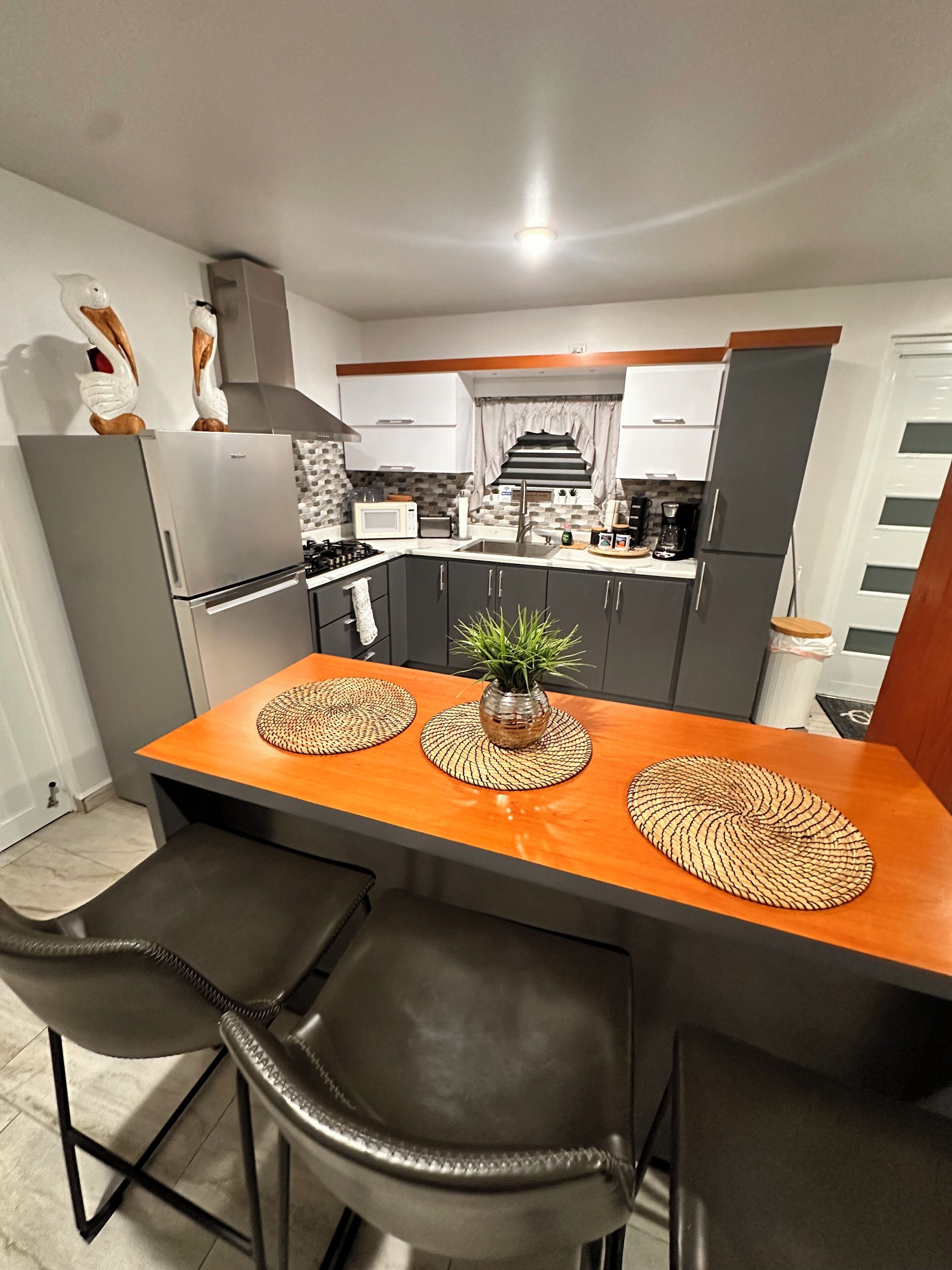 A modern kitchen with a central island, two chairs, a stove, and a refrigerator.