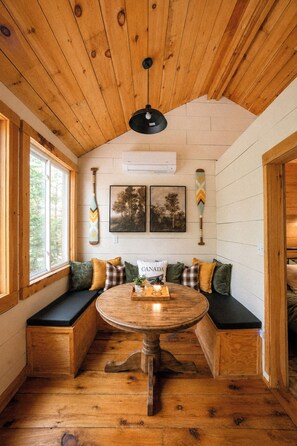 A cozy room with a wooden ceiling, a round table with a tray, and a bench with cushions. - Henrys cabin on the river (Northbrook)