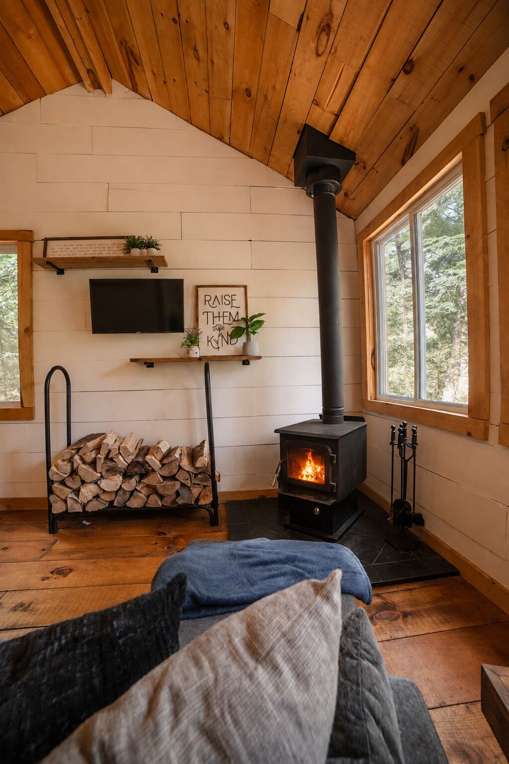 A cozy room with a fireplace, a television mounted on the wall, and a sign that reads 'RAISE THEM HIGH.'