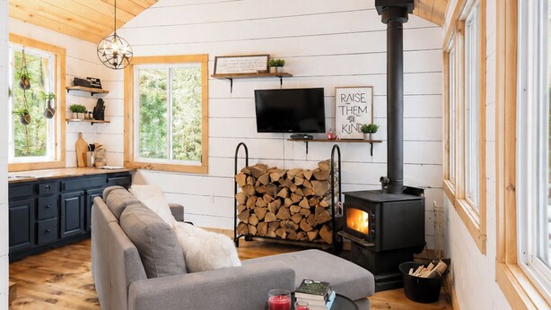 A cozy cabin interior with a sofa, a small table, a TV, a fireplace, and a window overlooking greenery. - Henrys cabin on the river (Northbrook)