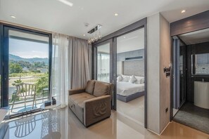 Ein modernes Hotelzimmer mit Balkon, Bett, Sofa und Bad mit Dusche und Toilette.