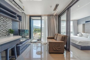 Ein modernes Hotelzimmer mit Balkon, einer Couch, einem Bett, einem Schreibtisch und Blick ins Freie.
