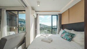 Une chambre d’hôtel comprenant un lit, un canapé, une grande fenêtre donnant sur la ville et un appareil de climatisation.