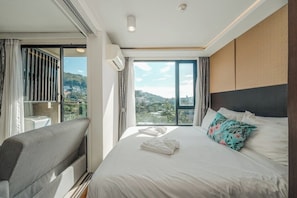 Ein Hotelzimmer mit Bett, Sofa, großem Fenster und Stadtblick sowie einer Klimaanlage.