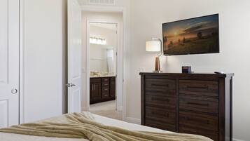 Un dormitorio con cama, cómoda, un cuadro y baño visible a través de una puerta abierta.