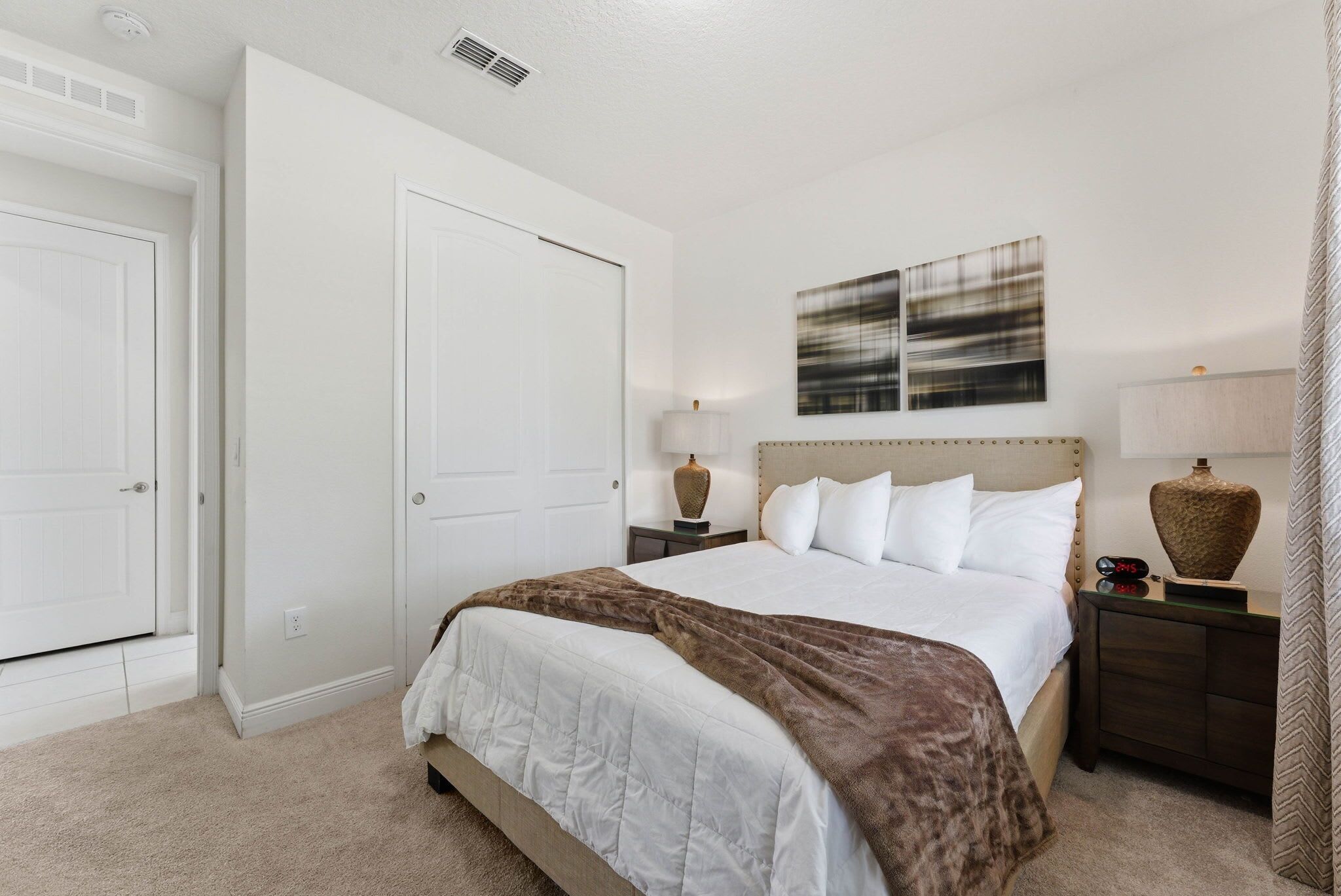 A bedroom with a bed, nightstands, a lamp, a painting, and a door.