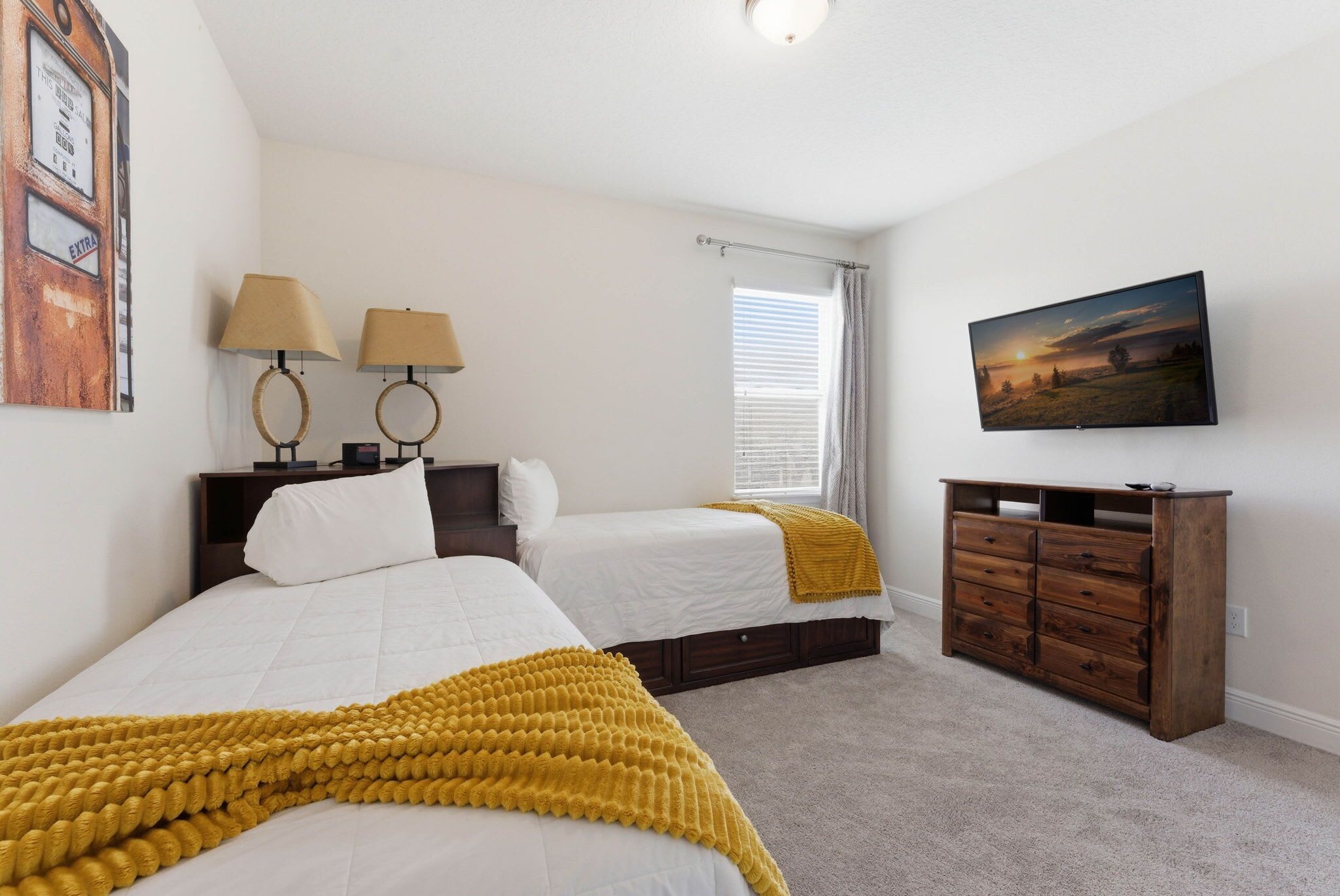 A bedroom with two beds, a dresser, a television, and a window with blinds.