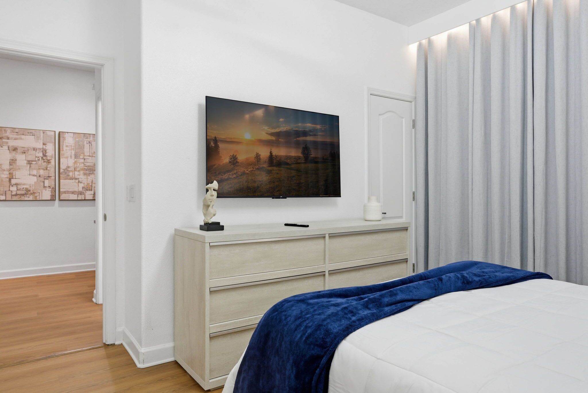 A bedroom with a bed, a dresser, a painting, and a door.