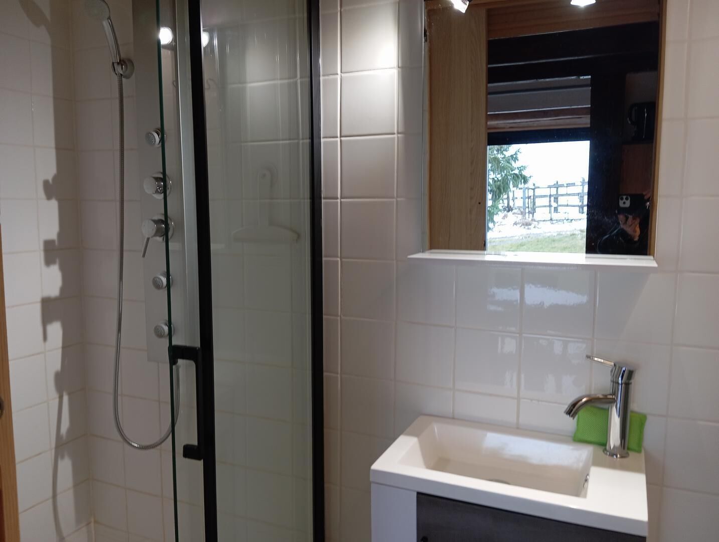 A bathroom with a glass-enclosed shower, a white sink, and a window with a view of the outside.