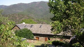 Un bâtiment en pierre doté d’un toit en pente, entouré de verdure et avec des montagnes en arrière-plan.