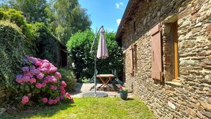 Un bâtiment en pierre avec un jardin, une table entourée de chaises et une pergola.