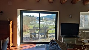 A living room with a sliding glass door to a patio, a television, a radiator, and a wooden ceiling. - Balcon des Fées - MALZIEU VILLE (LE) (MALZIEU VILLE (LE))