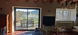 Ein Wohnzimmer mit einer Schiebeglasdoor zum Patio, einem Fernseher, einem Heizkörper und einer Holzbalkendecke.