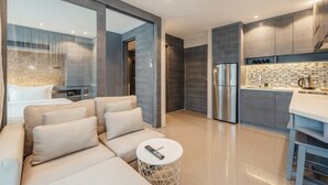 Moderni sisustus, jossa on sohva, pyöreä sohvapöytä, keittiöalue jääkaapilla ja laatoitettu seinä keittiötason yläpuolella.