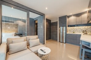 Ein modernes Interieur mit einer Couch, einem runden Couchtisch, einer Küchenzeile mit Kühlschrank und einer gefliesten Spritzschutzwand.