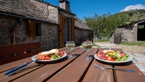 Edificio de piedra rústico con una mesa de madera dispuesta para una comida, mostrando platos de comida y copas de vino.