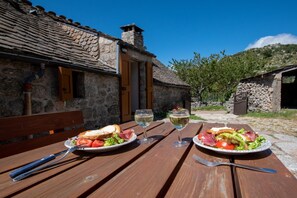 Ein rustikales Steinhaus mit einem Holztisch, gedeckt für eine Mahlzeit, mit Tellern voller Speisen und Weingläsern.