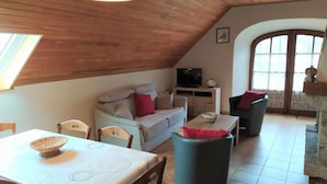Un acogedor espacio tipo loft con techo alto, un sofá, una mesa de comedor y un televisor.