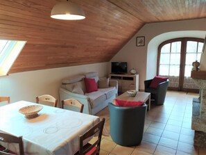 Ein gemütliches Loft mit hohen Decken, einer Couch, einem Esstisch und einem Fernseher.