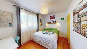 Un dormitorio con cama, mapa, lámpara y un póster con vista a la ciudad.