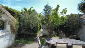 Un patio con una mesa redonda y sillas, rodeado de follaje y un muro de piedra.